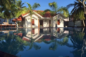 A pool with a reflection of palm trees and a building with a red roof and white walls. - Sisikirana Villa (Unawatuna)