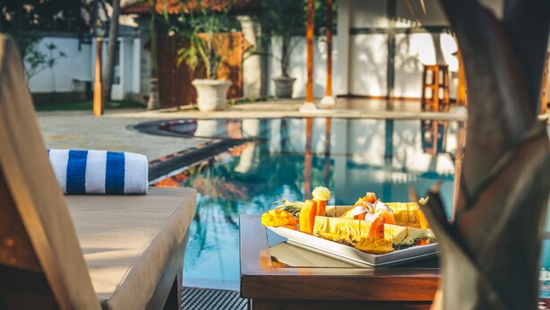 A poolside setting with a table set for a meal, a lounge chair, and a view of a pool and garden. - Sisikirana Villa (Unawatuna)