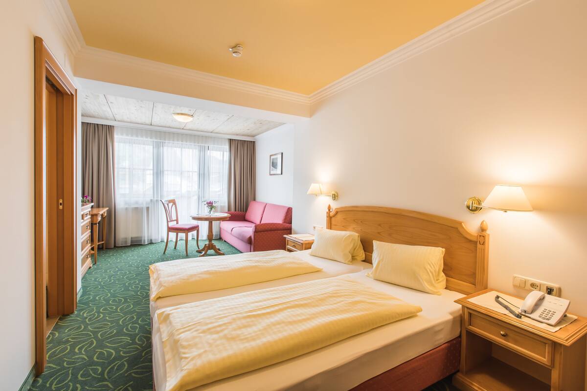A hotel room with two beds, a desk, a chair, a small table, and a red sofa.