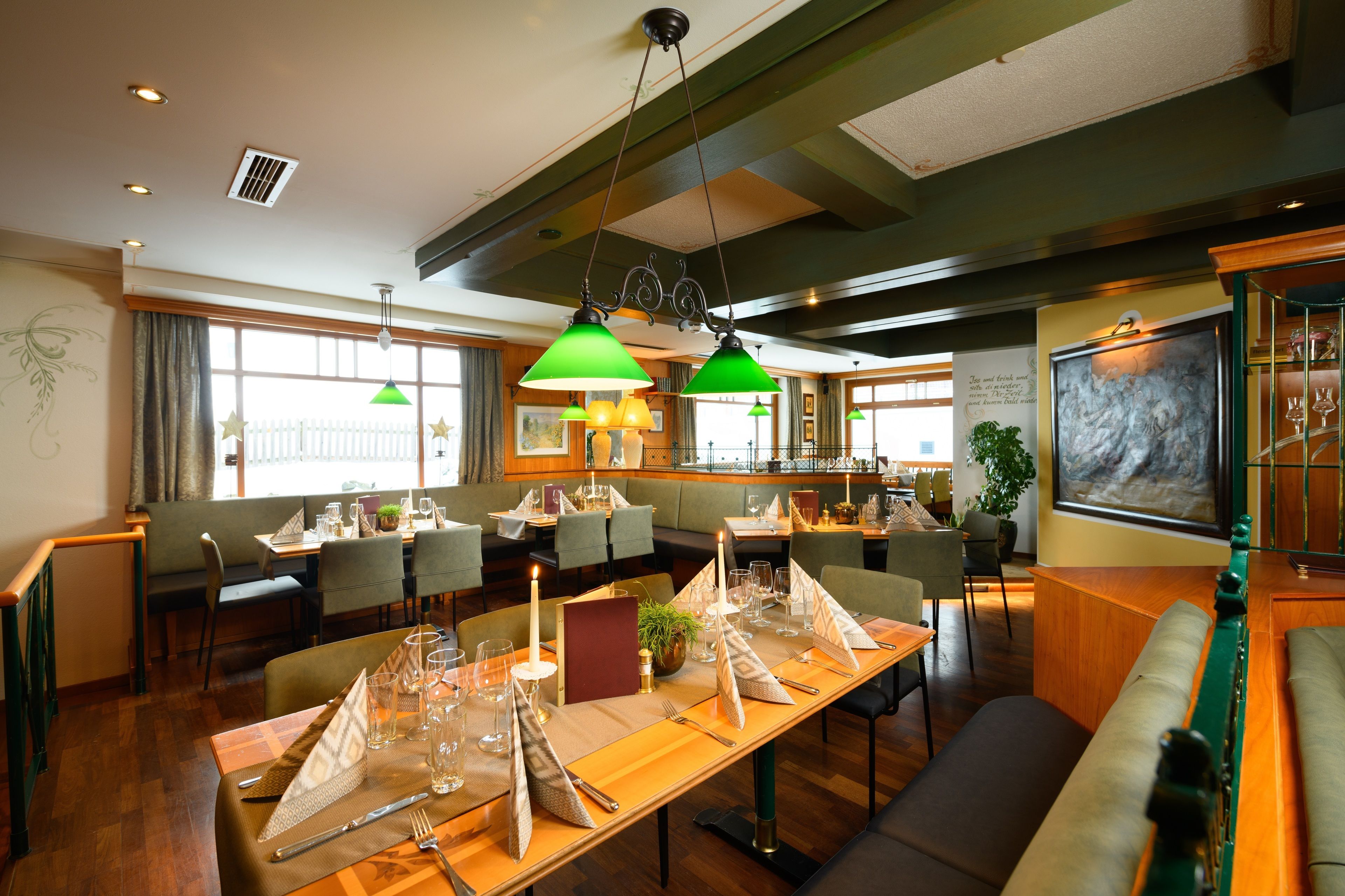 A restaurant with multiple dining tables set for guests, featuring green pendant lighting and a large painting on the wall.