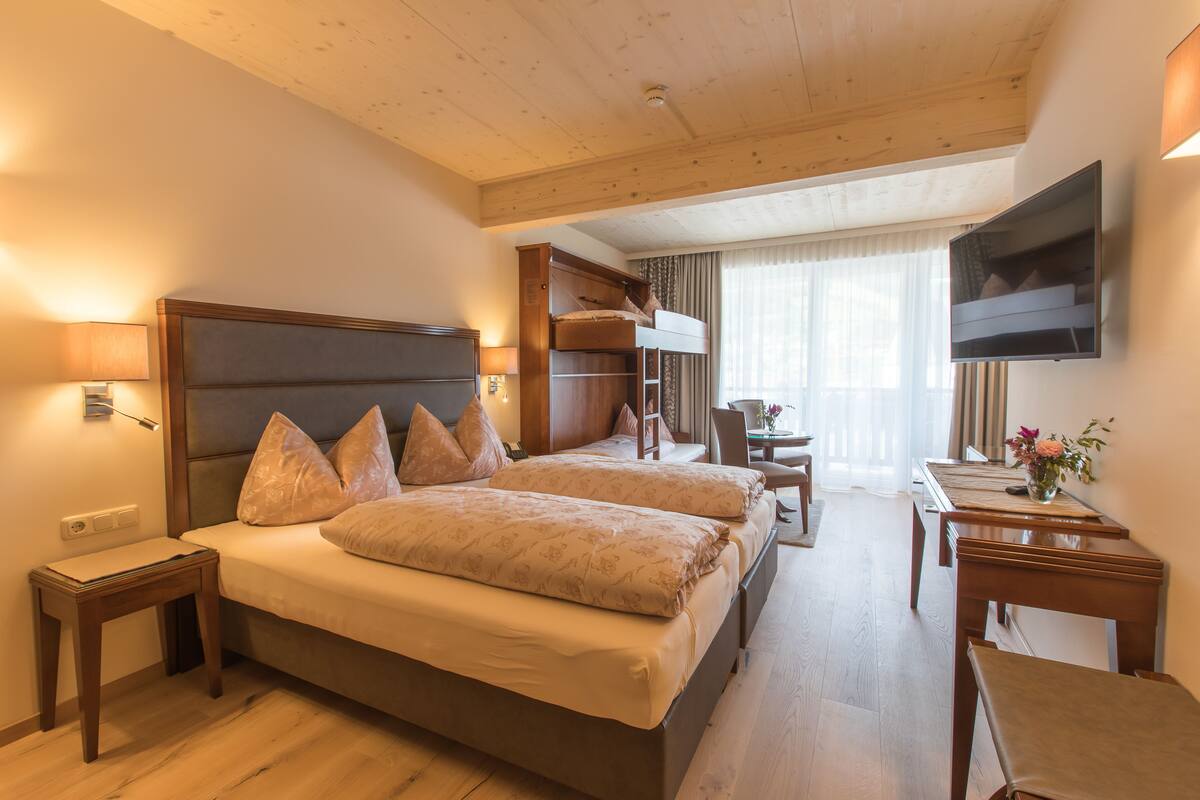 A hotel room with a large bed, a desk, a TV, and a balcony.