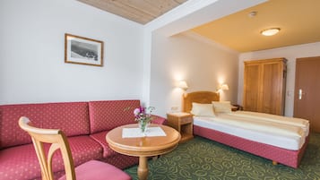 Een hotelkamer met een bed, een rode bank, een houten stoel, een kleine tafel met een vaas en een lijst met een foto aan de muur.