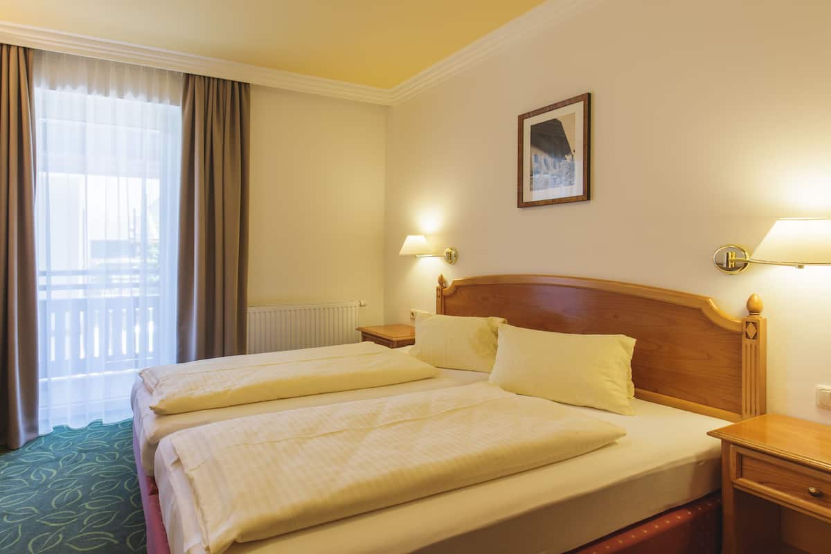 A hotel room with a double bed, two bedside tables, a chair, a window with curtains, and a wall-mounted picture.