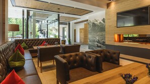 A modern interior with a wooden ceiling, a large flat-screen TV, and a seating area with leather sofas and a wooden table. - Hotel Niederreiter (Maria Alm am Steinernen Meer)