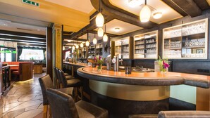 A bar area with a curved counter, bar stools, and hanging pendant lights. - Hotel Niederreiter (Maria Alm am Steinernen Meer)