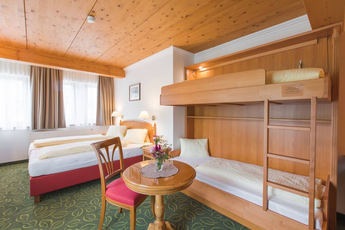 A hotel room with a bed, a desk, a chair, and a bunk bed.