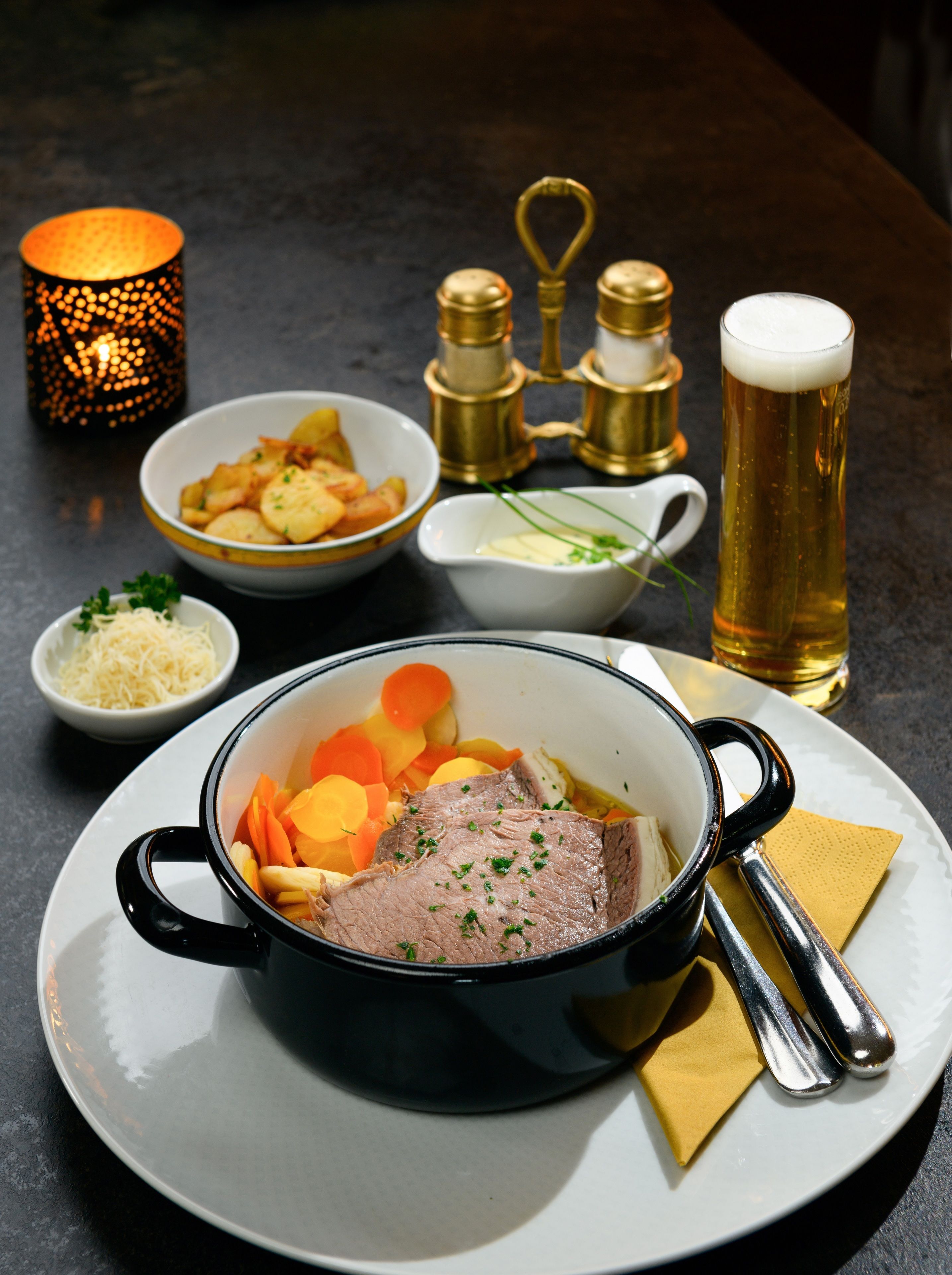 A dining table with a roast beef dish, vegetables, and a beer glass.