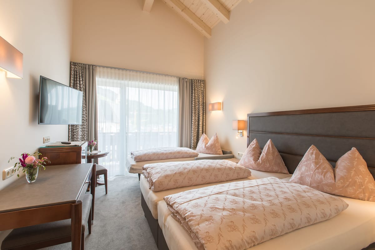 A hotel room with a large bed, a smaller bed, a desk with a chair, a TV, and a window with curtains.