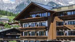 A hotel with a wooden facade, balconies with flower boxes, and a mountain backdrop. - Hotel Niederreiter (Maria Alm am Steinernen Meer)