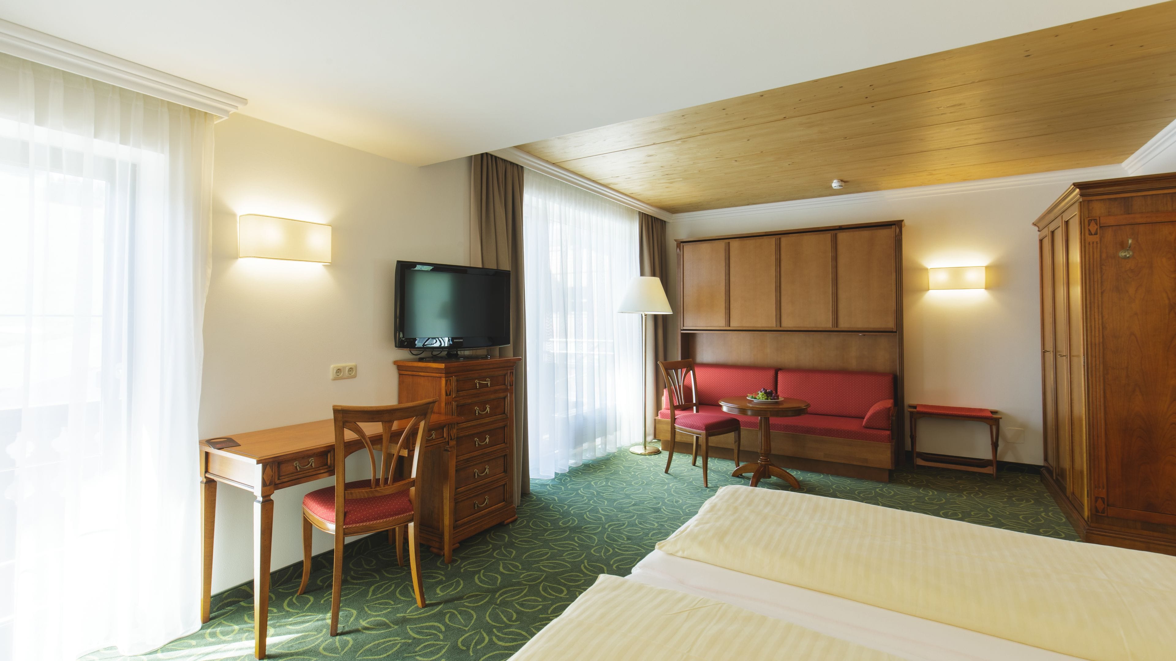 Una habitación de hotel con una cama, un escritorio con una silla, un televisor, un sofá y un armario.