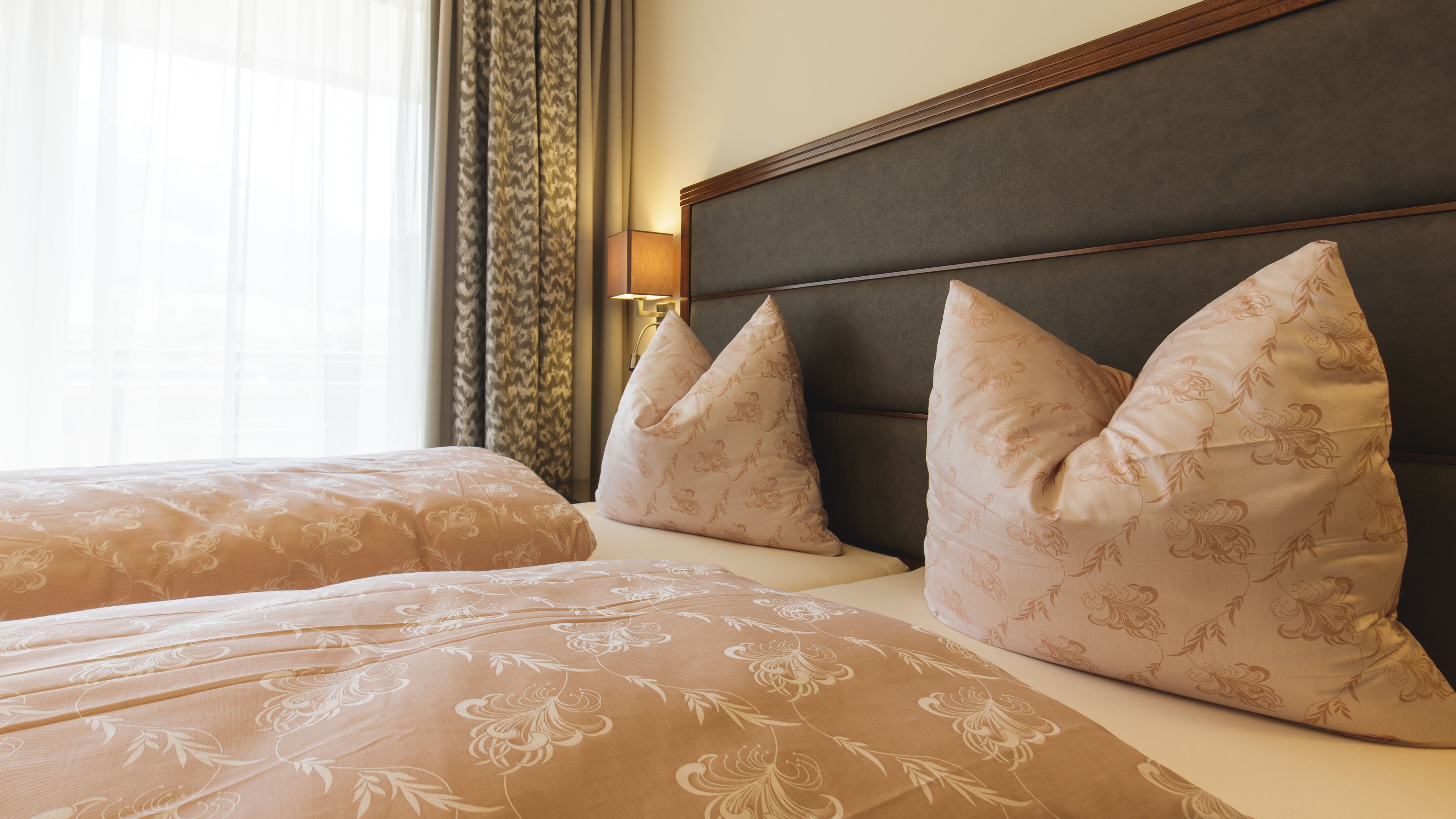 A hotel room with two beds, each with floral-patterned bedding and matching pillows.