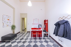 A room with a checkered floor, a desk with two chairs, a bulletin board, a coat rack, and a bench. - Mamamia Hostel and Guesthouse (Palermo)