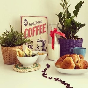 A breakfast setup with a coffee sign, a plant, a bowl of cereal, a milk bottle, a blue mug, and a plate of croissants. - Mamamia Hostel and Guesthouse (Palermo)