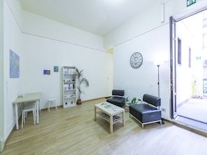 A reception area with a wooden floor, a reception desk, a bookshelf, a clock, and a seating area with chairs and a table. - Mamamia Hostel and Guesthouse (Palermo)
