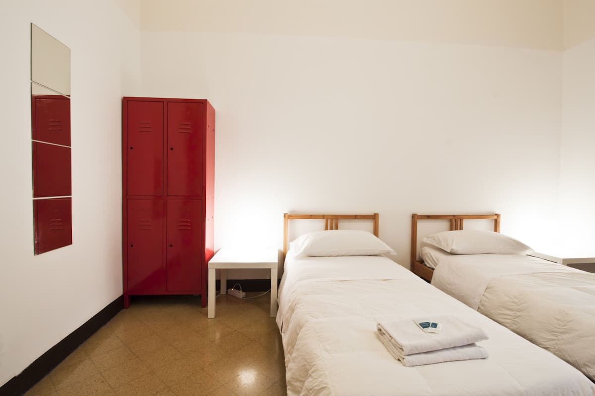 A room with two single beds, a red wardrobe, a small table, and a mirror on the wall.