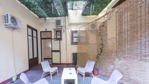A room with four white chairs around a small table, a potted plant, and a wall with a woven texture. - Mamamia Hostel and Guesthouse (Palermo)