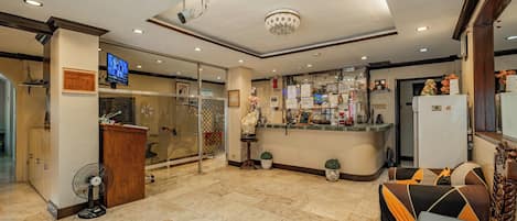 A hotel lobby with a reception desk, a TV, and a seating area with a sofa and chairs.