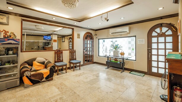 A hotel lobby with a reception desk, a seating area with a sofa and chairs, a large mirror, and a view of the outside through a window. - Hotel Juliano (Manila)