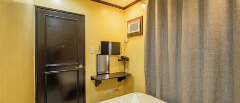 A hotel room with a bed, a flat-screen TV, a coffee machine, and a wall-mounted phone.