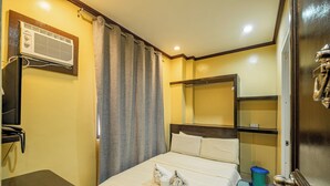 A hotel room with a bed, a small table, a trash bin, and an air conditioning unit. - Hotel Juliano (Manila)