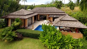 A house with a pool, surrounded by lush greenery and palm trees.