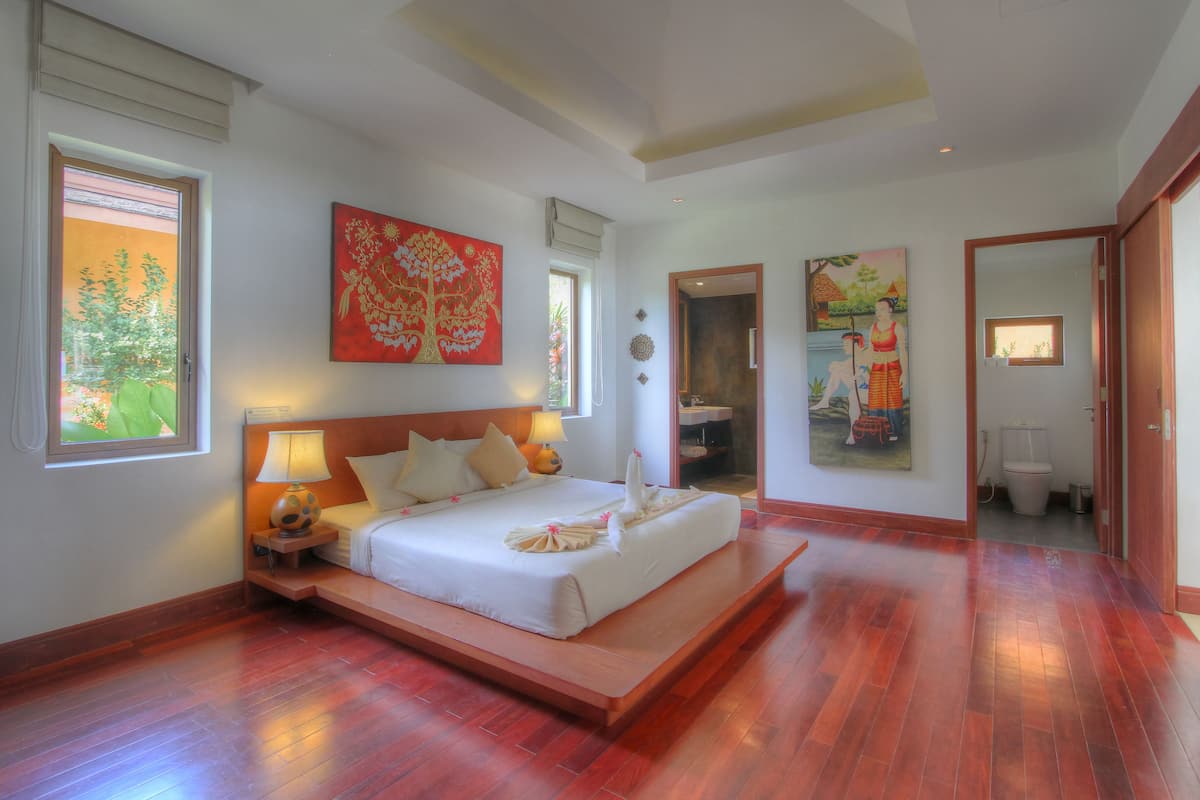Une chambre spacieuse avec un grand lit, une table de chevet et une fenêtre donnant sur un paysage verdoyant.
