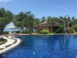 Une piscine dotée d’une terrasse carrelée, entourée de palmiers et bordée d’un bâtiment dont le toit est également recouvert de tuiles.