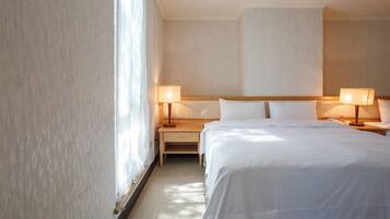 Hotelkamer met een groot bed, twee nachtkastjes met lampen, een bijzettafeltje en een raam met dunne gordijnen.