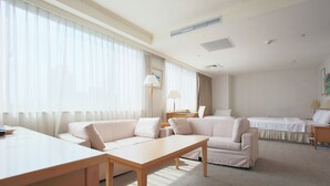 Una habitación de hotel con un ventanal grande, un sofá, una cama, un escritorio y una lámpara.