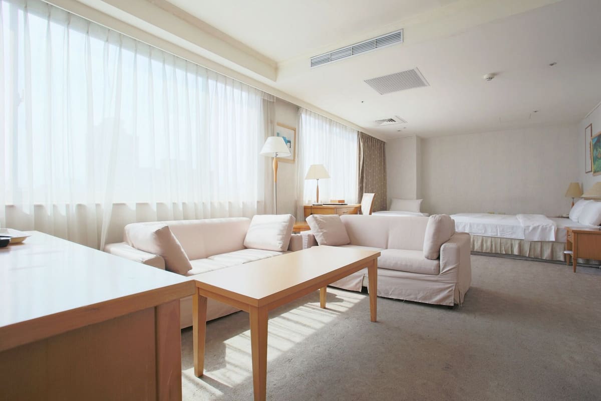 Een hotelkamer met een groot raam, een bank, een bed, een bureau en een lamp.