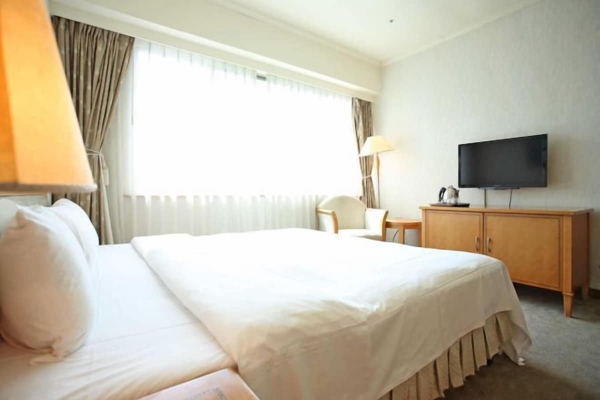 A hotel room with a large bed, a television, a desk, and a chair.