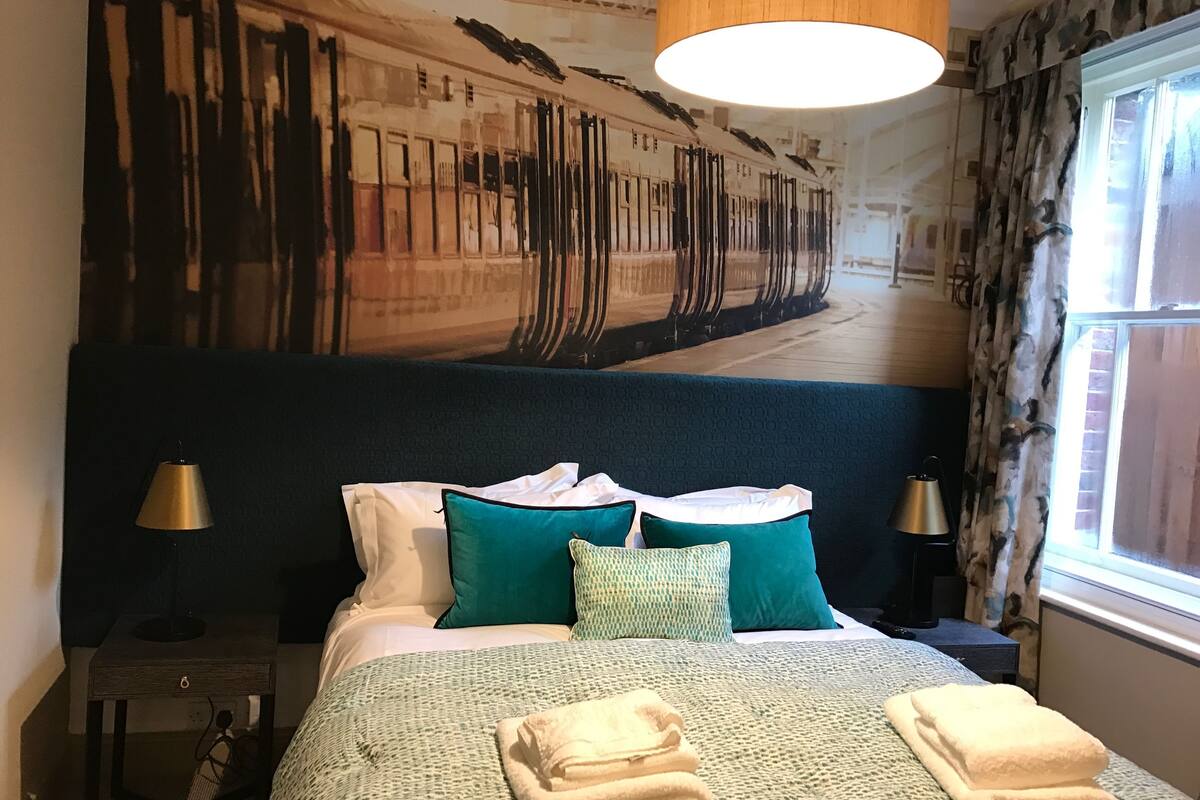 A hotel room with a large bed, a headboard with a mural, two bedside tables with lamps, and a window with curtains.