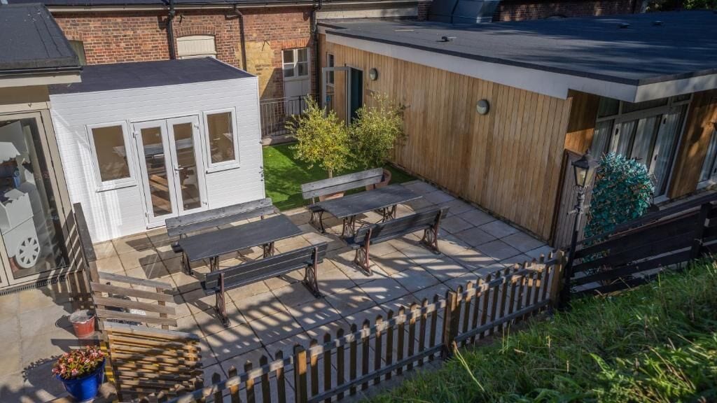 A patio area with a wooden deck, a small white structure, and a bench.