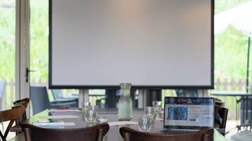 Un salón de conferencias con una pantalla grande, sillas de madera, una mesa de vidrio y un ordenador portátil mostrando una presentación.