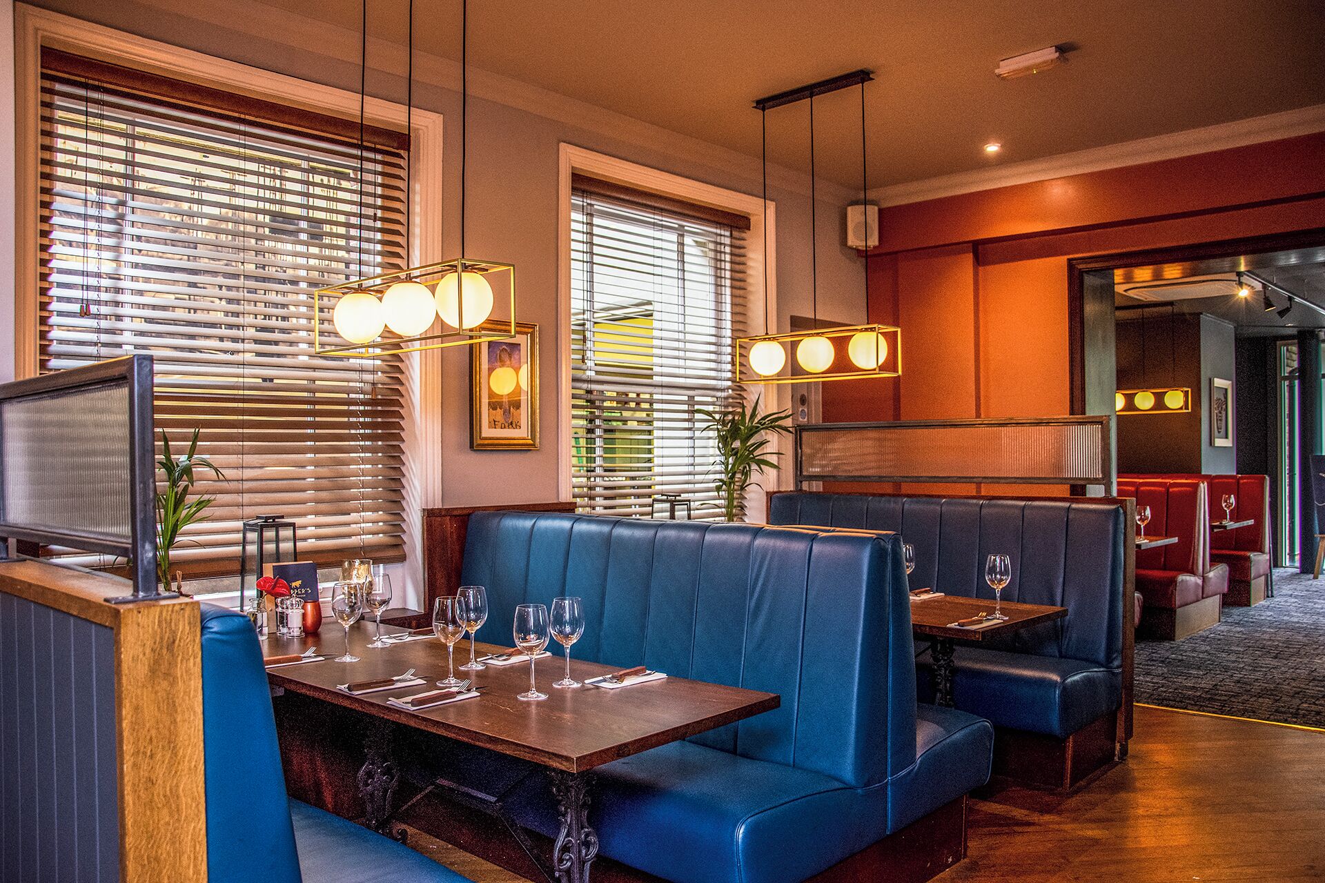 A restaurant with booths and tables, large windows with blinds, and hanging pendant lights.