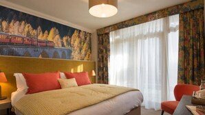 Une chambre d’hôtel avec un grand lit, un bureau, une chaise et un tableau représentant un train accroché au mur.