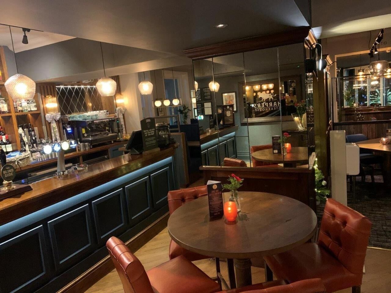 A bar area with a round table and leather chairs, a bar counter with various bottles, and hanging pendant lights.