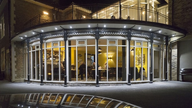 Un bâtiment d’angle doté d’une façade vitrée, d’un balcon et dont le sol reflète une voiture.