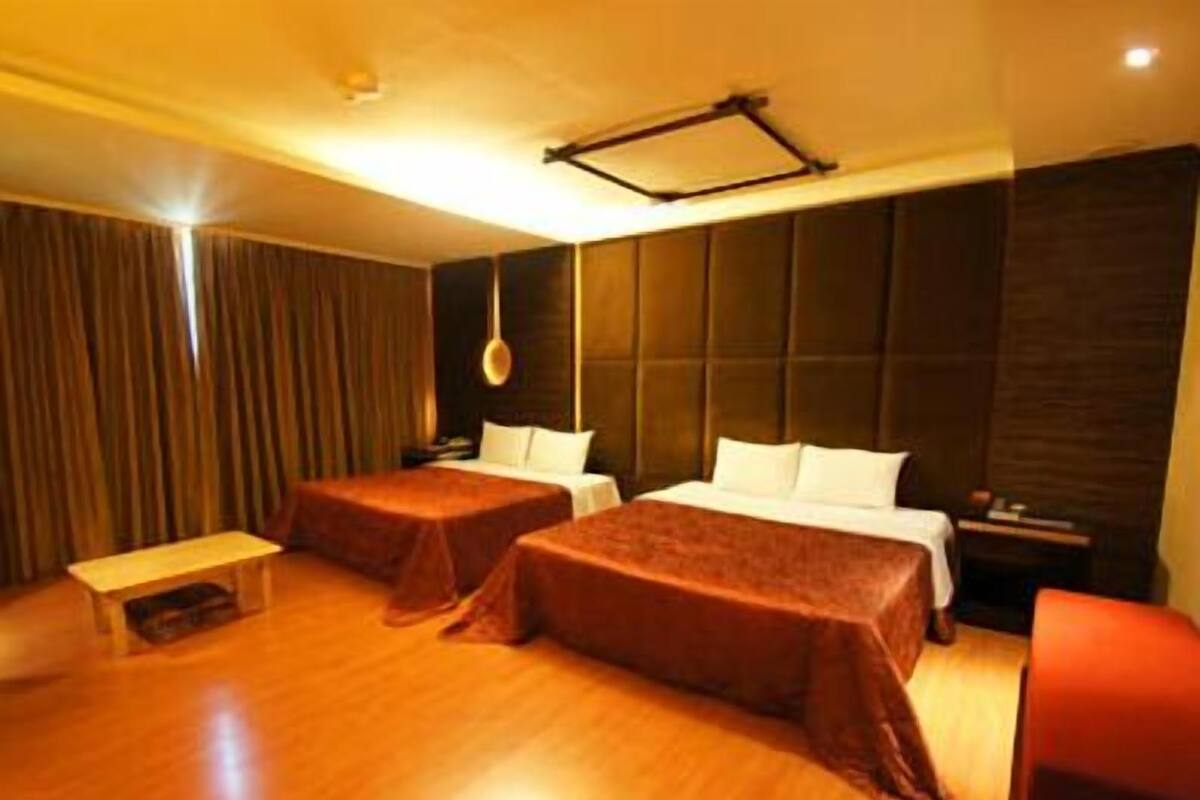 A hotel room with two beds, a small table, and a hanging light fixture.
