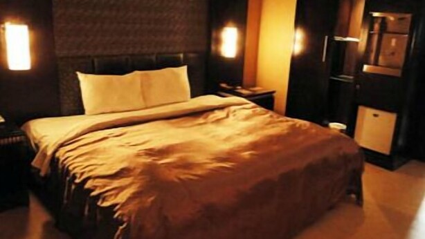 Una cama bien hecha con cabecera, una mesita de noche y una mesita auxiliar.
