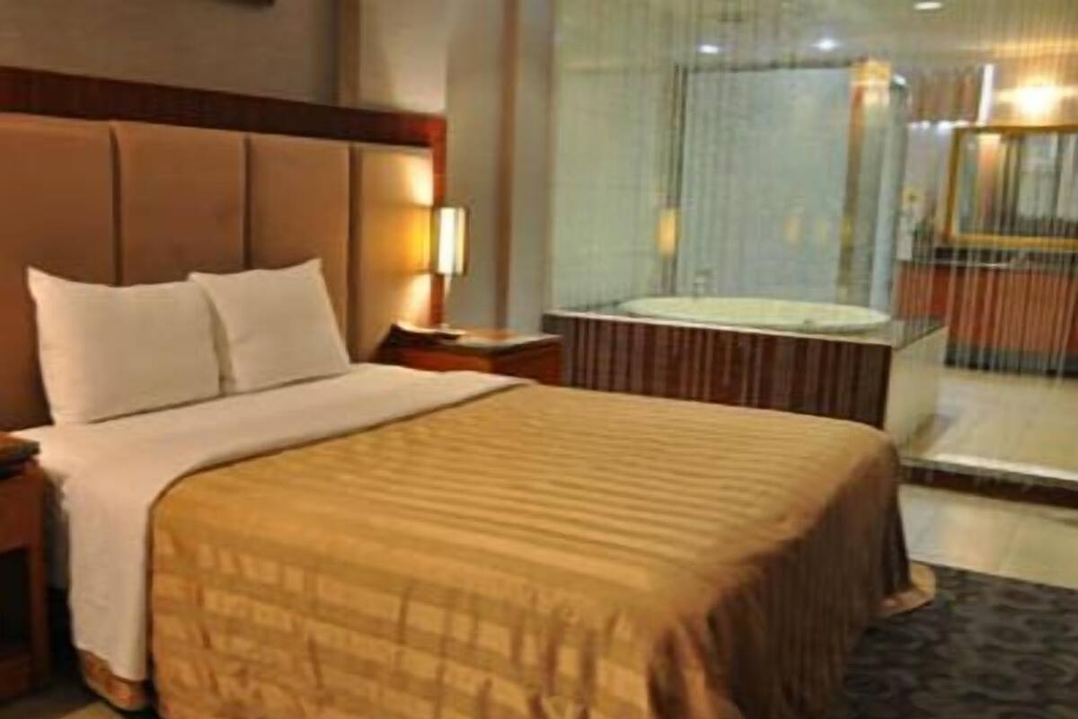 A hotel room with a large bed, a bedside table, a lamp, and a view of a pool area.