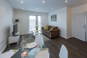 Un salon moderne avec un canapé, une table à manger pour deux personnes et un téléviseur posé sur un meuble.