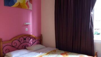 A bedroom with a bed, a pink wall, a painting, and a window with curtains.