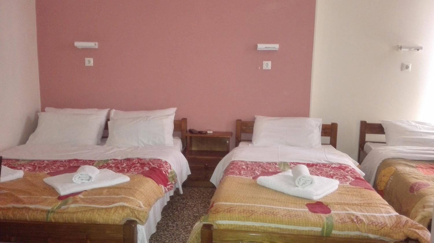 A hotel room with two single beds, each with a neatly folded towel and a floral-patterned bedspread.