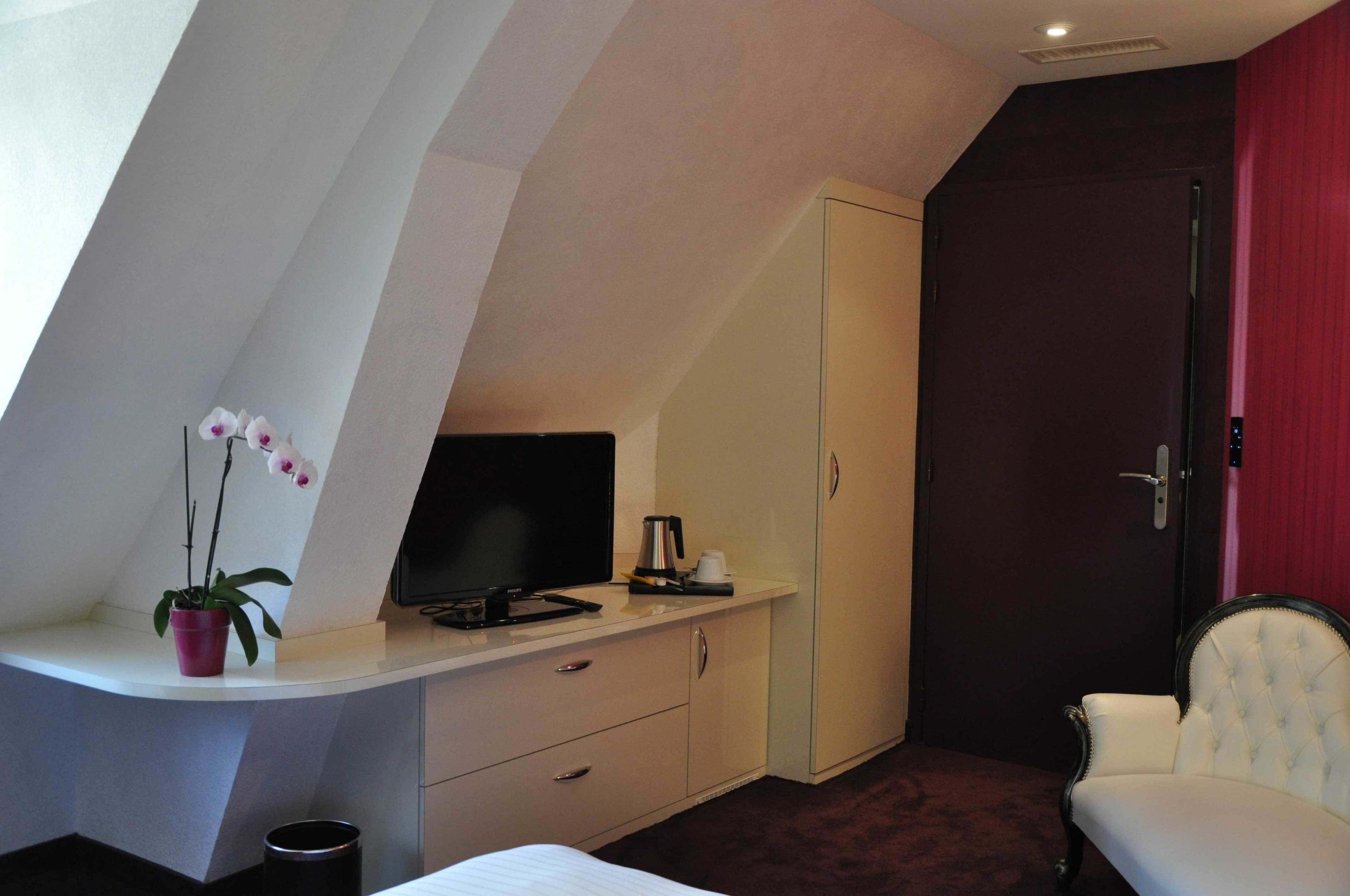 A room with a bed, a TV, a desk with a plant, a wardrobe, and a red door.