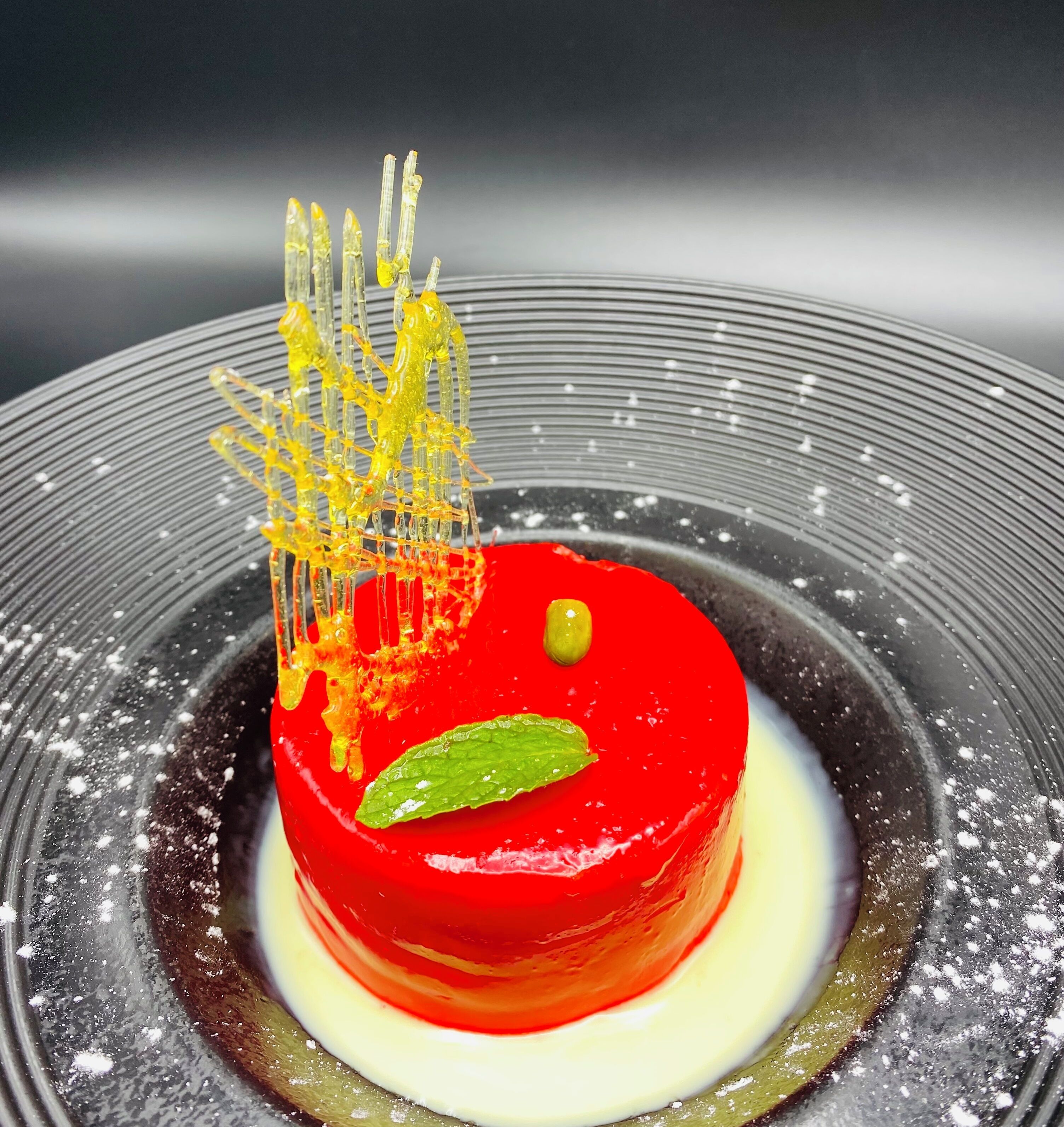 Un dessert composé d’une base rouge, d’une feuille verte et d’une structure jaune, le tout présenté sur une assiette.