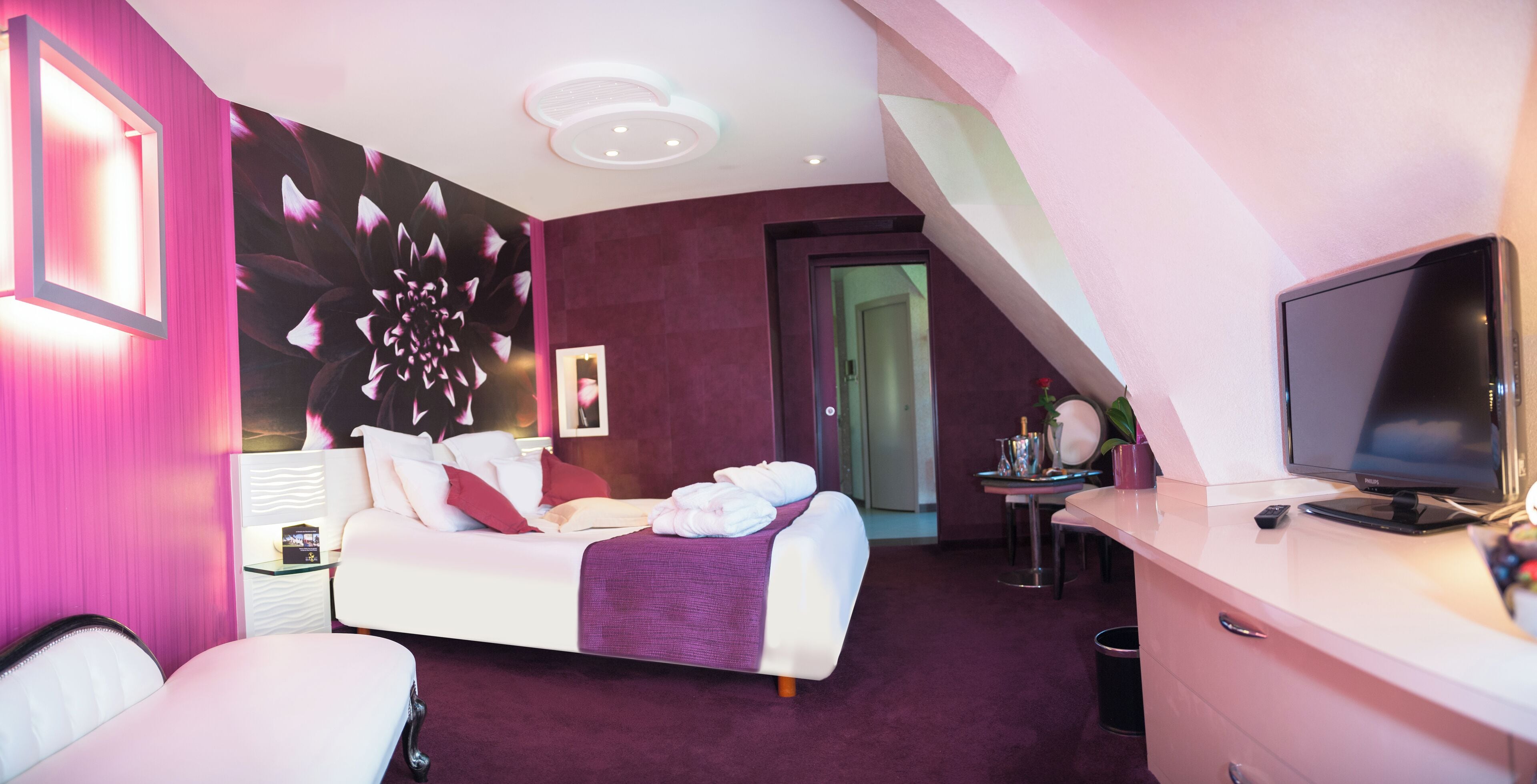 Une chambre d’hôtel moderne équipée d’un lit, d’un bureau avec une télévision et d’une grande fresque murale à motifs floraux.