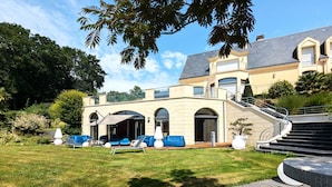A modern house with a spacious outdoor seating area, a staircase leading to a balcony, and a well-maintained lawn.