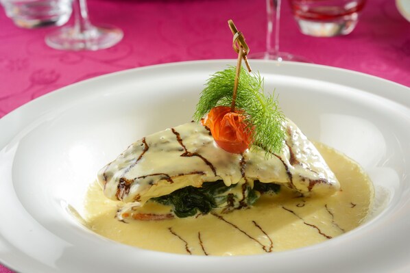 Un plato blanco con un guiso de carne, verduras y una guarnición sobre un mantel rosa.