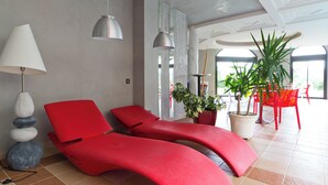 A modern spa room with two red lounge chairs, a white lamp, and a large potted plant.